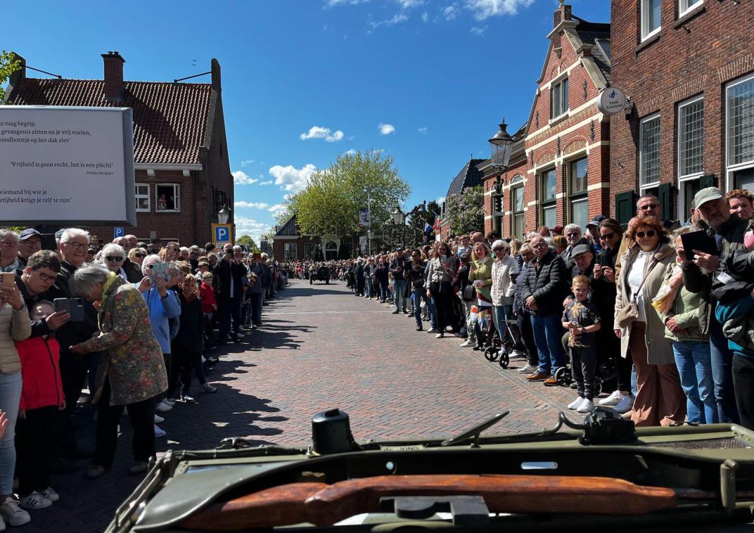 Auto rijdt door de straat, langs de beide kanten van de straat staan allemaal mensen die een soort doorgang maken voor de auto