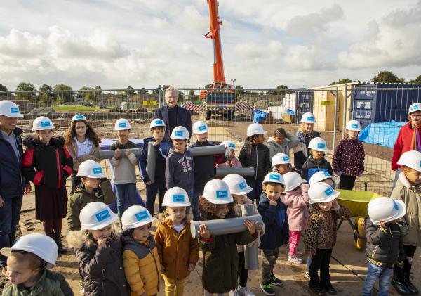 Kinderen staan op de bouwplaats met bouwhelmen op en capsules in hun hand.