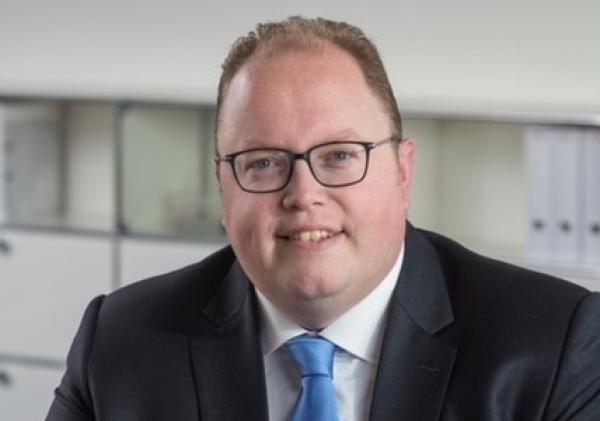 De kroonbenoemde burgemeester Ben Visser glimlachend aan tafel met zijn handen over elkaar