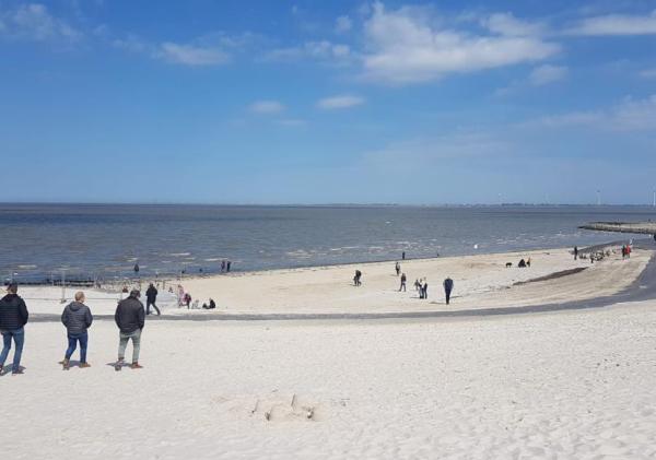Een brede foto van het stadsstrand van Delfzijl met een aantal mensen die over het strand lopen.