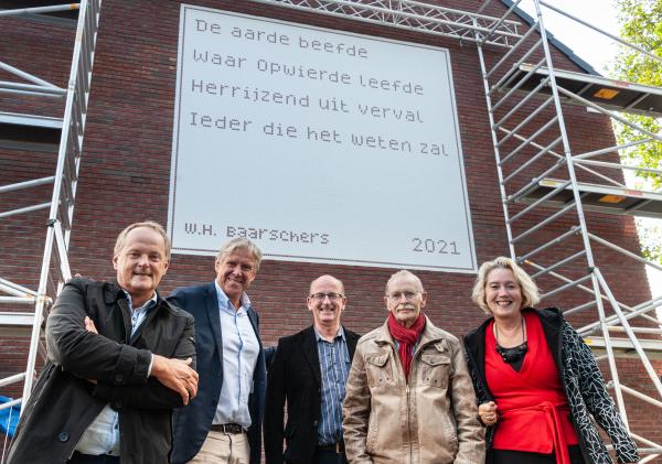 De personen die de onthulling deden poseren voor het gedicht aan de muur