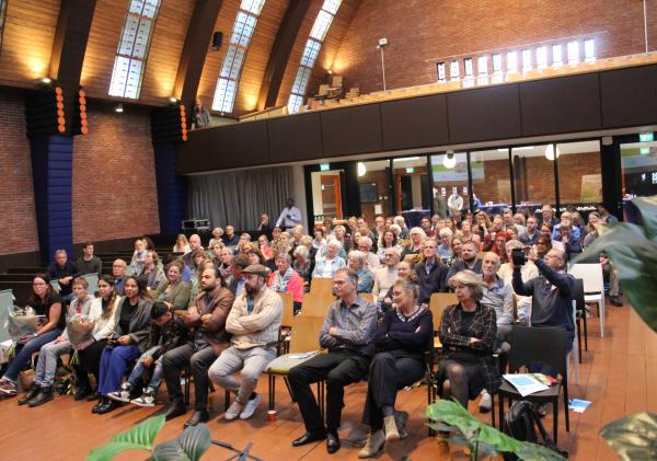 Een groepsfoto van bezoekers die op stoelen zitten, tijdens een symposium over eenzaamheid.