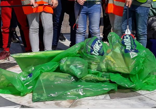 Een groepje mensen staat om groene zakken met zwerfafval.
