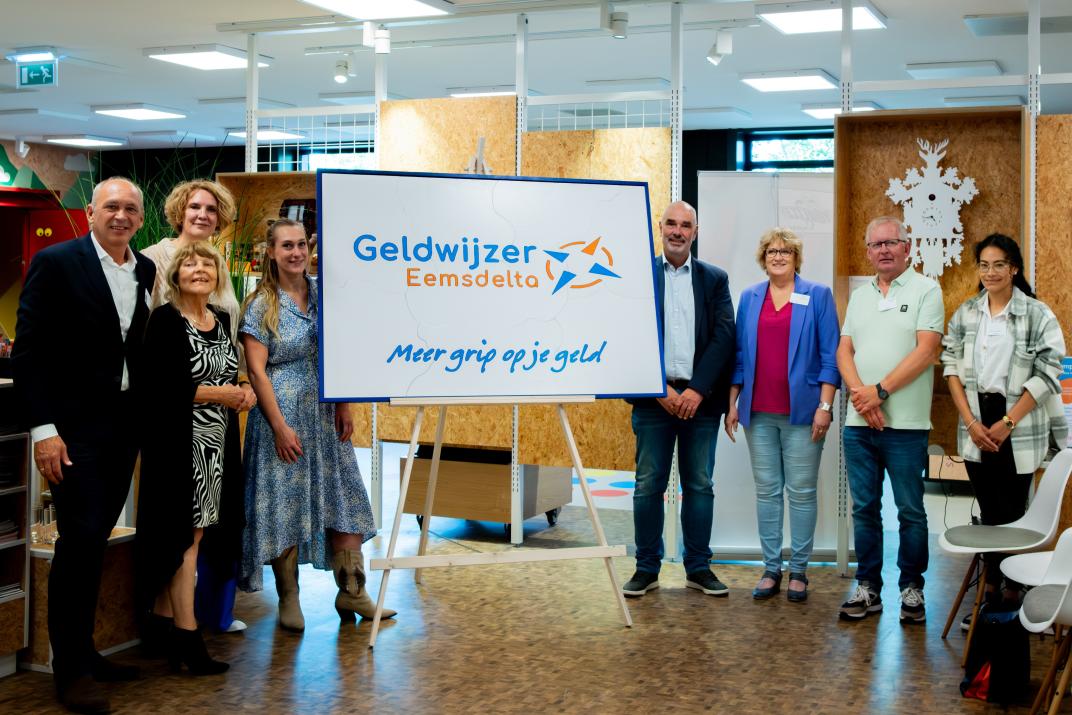 Vertegenwoordigers van de ketenpartners van Geldwijzer Eemsdelta staan naast het logo dat wordt onthuld