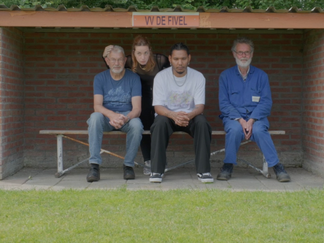 4 mensen zitten in de dug-out op het voetbalveld